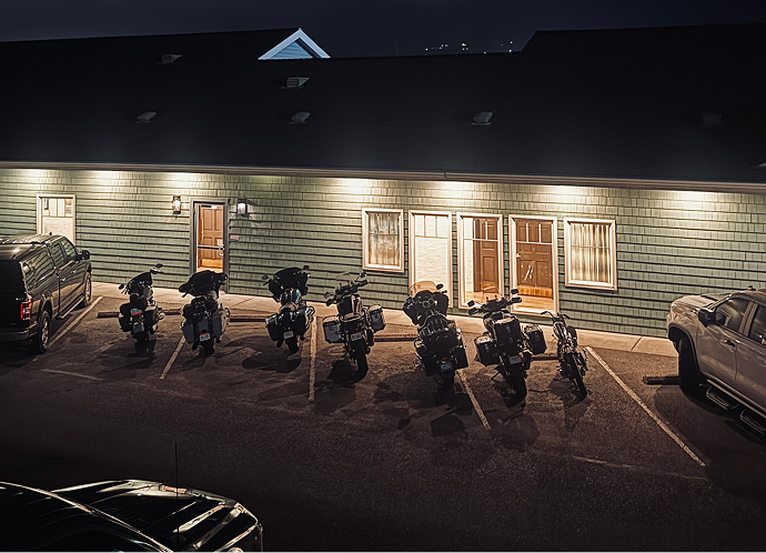 Row of motorcycles parked outside a motel at night under exterior lights in a quiet parking lot
