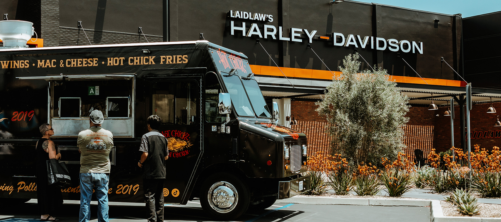 People order from a food cart that is parked in front of the Laidlaw’s Harley-Davidson dealership.