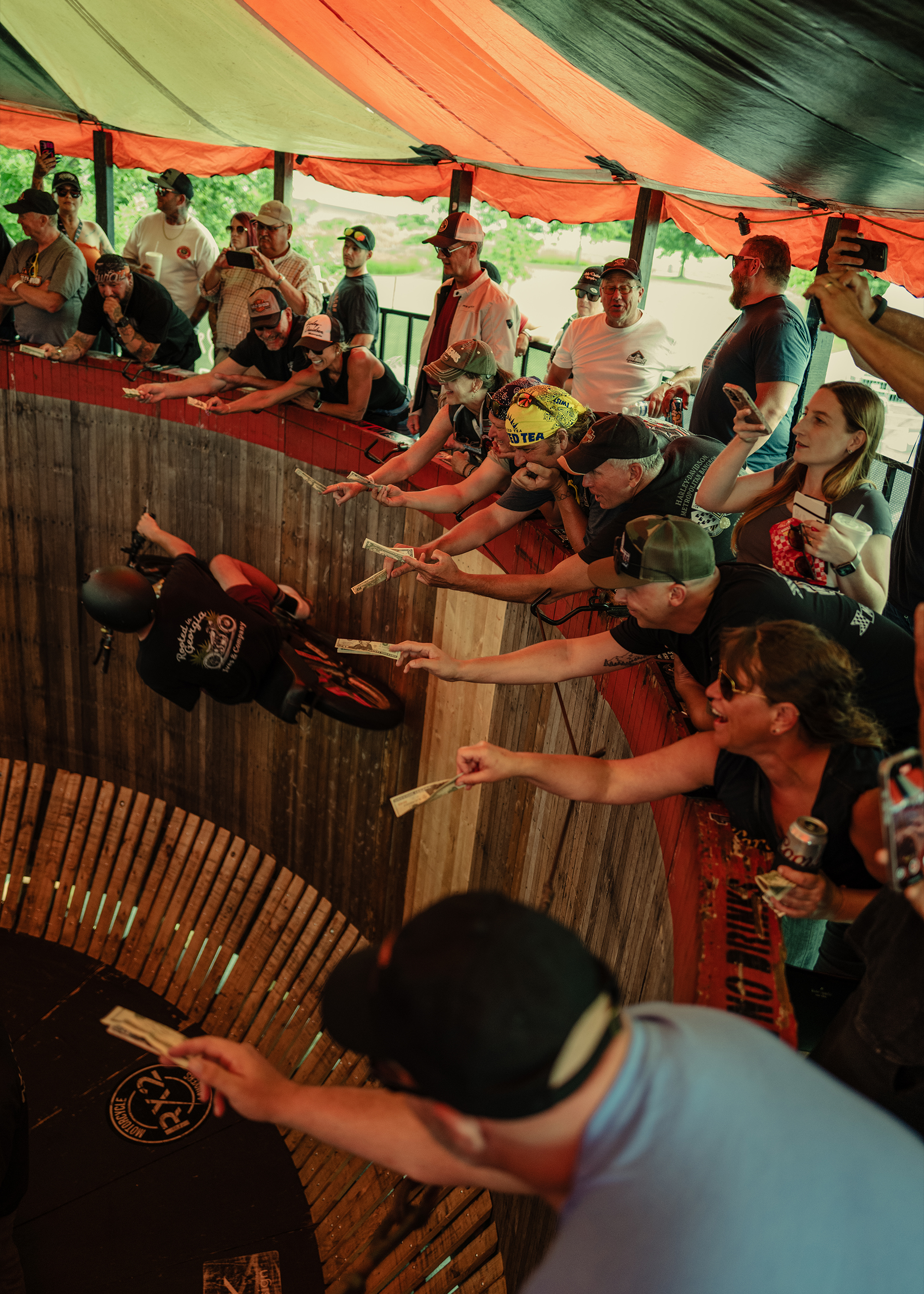 A motorcycle travels around the wall of death as the audience reaches out with money for him to grab