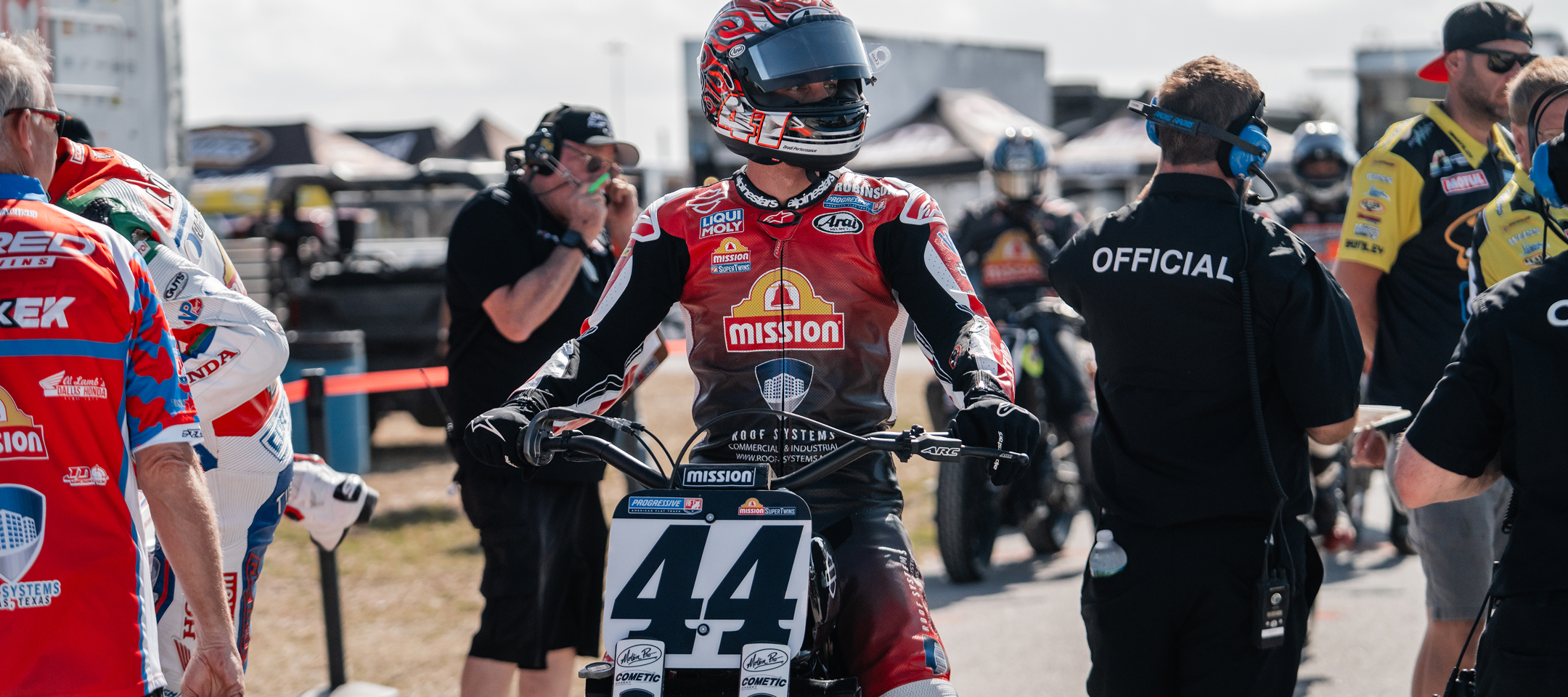Brandon Robinson aboard bike #44 waits in the paddock before a flat track race, surrounded by crew and officials