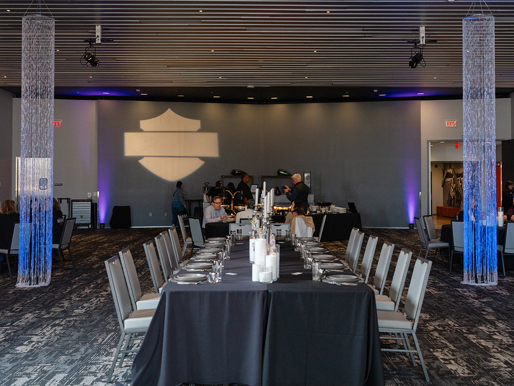 Long banquet table setup with chairs and Harley-Davidson logo projection in event hall