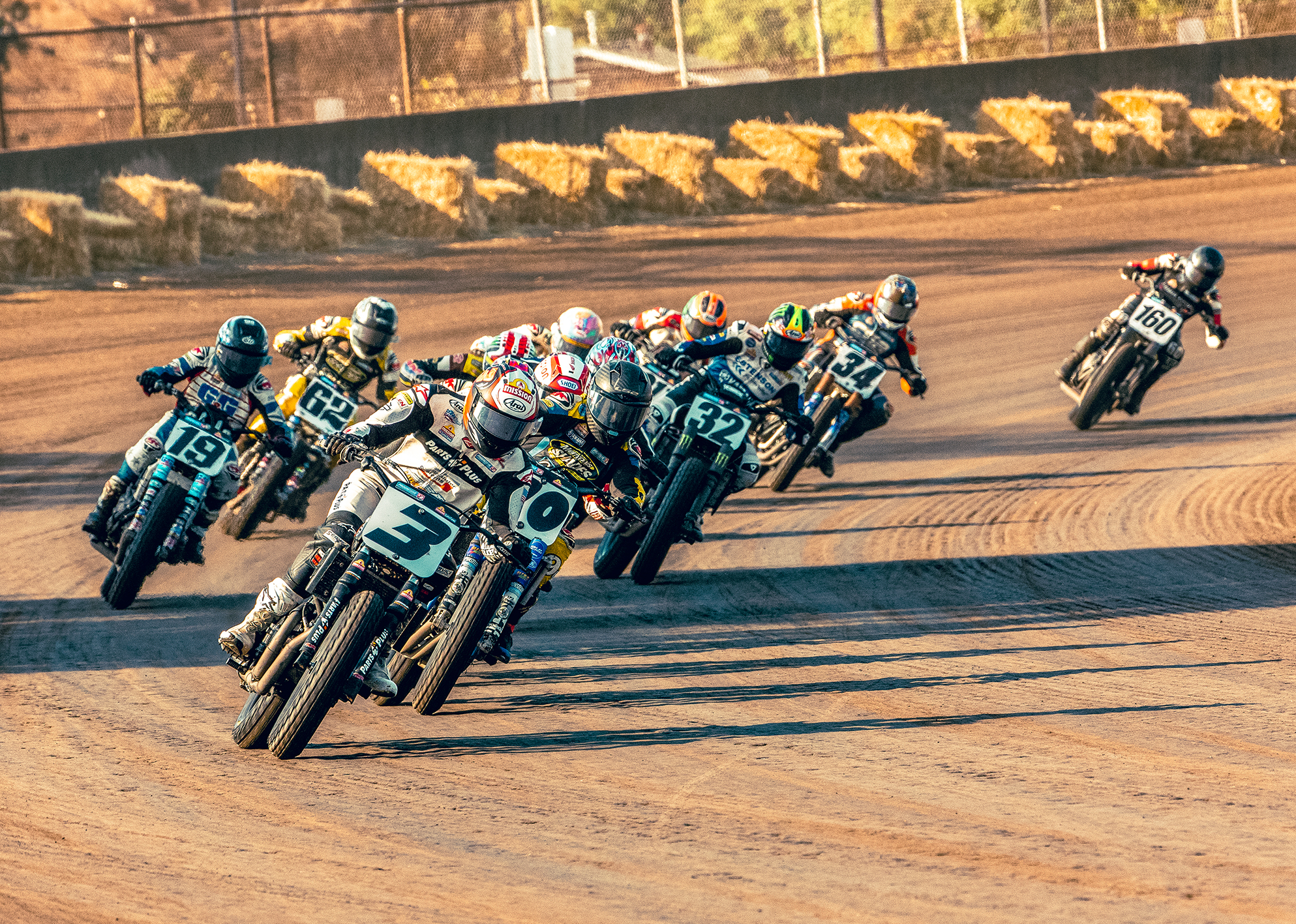 A group of motorcycle racers led by number 3 Briar Bauman leans into a dirt track curve during a competitive race