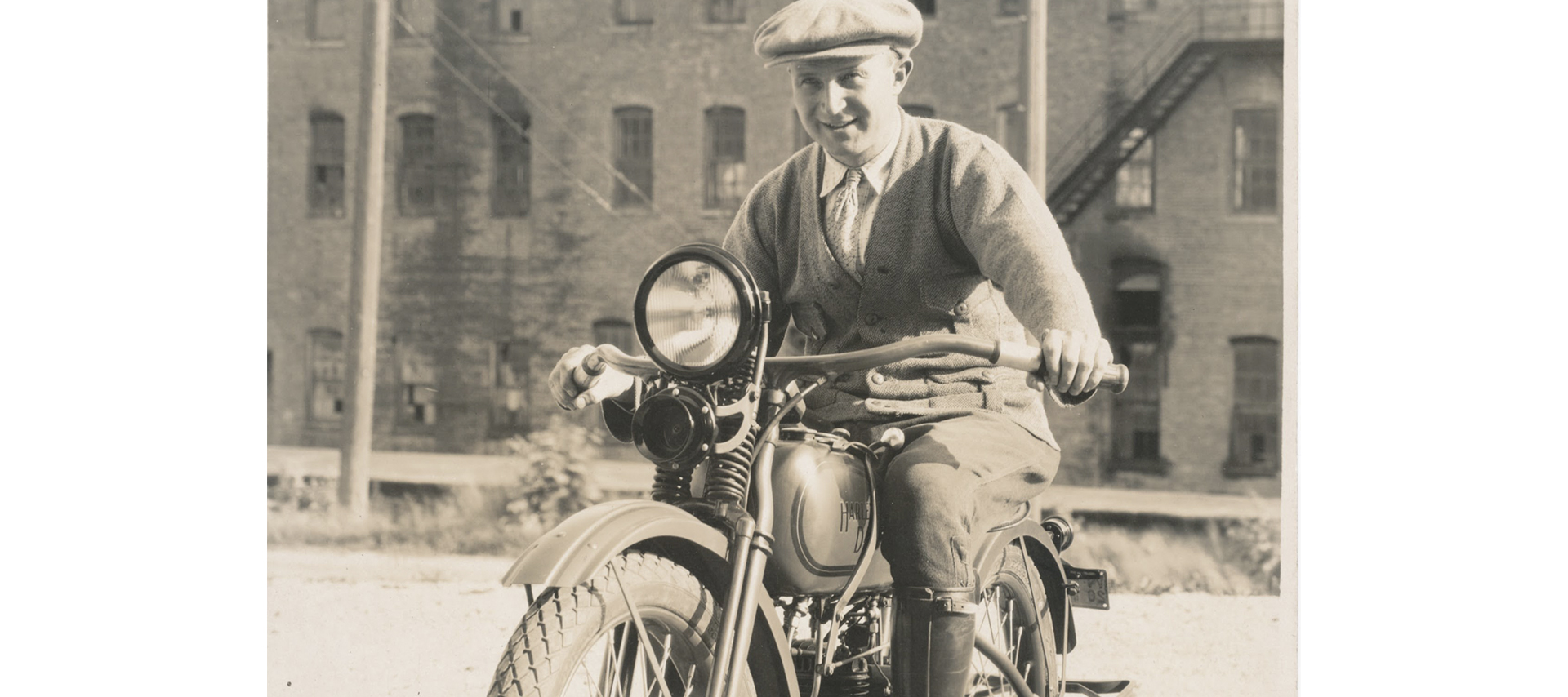 A man in a cap smiles astride a motorcycle 