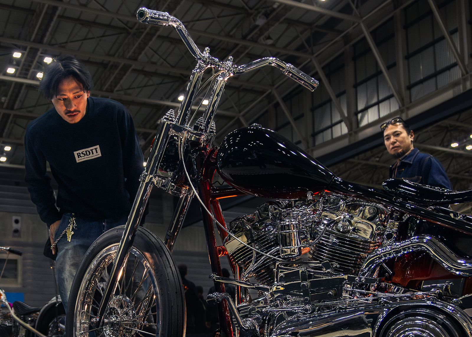 Onlookers check-out a custom Harley-Davidson chopper with chrome detailing and deep ruby paint