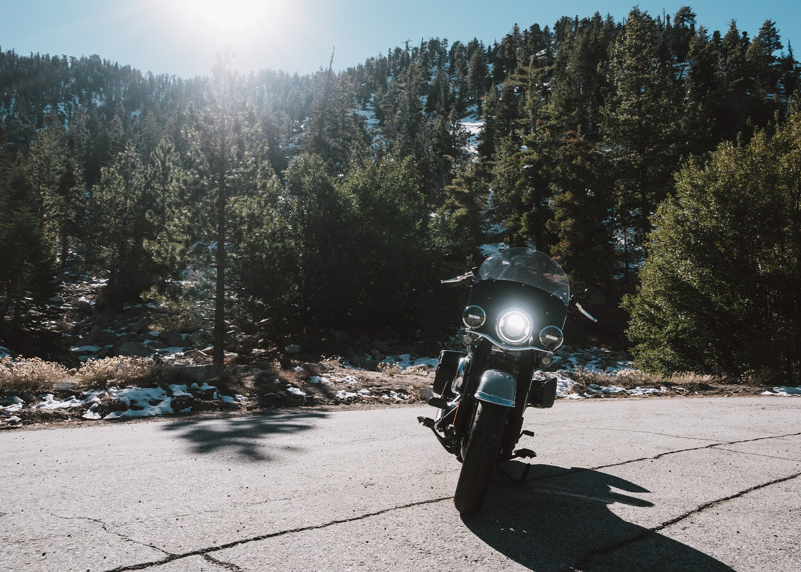Front view of a Harley-Davidson Heritage Classic motorcycle parked in front of mountains covered with evergreens and patches of snow