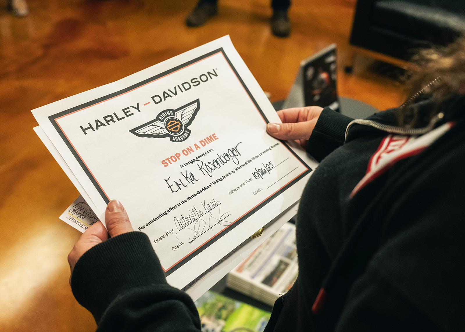 Looking over the shoulder of a student holding a “Stop on a dime” H-D Riding Academy certificate.