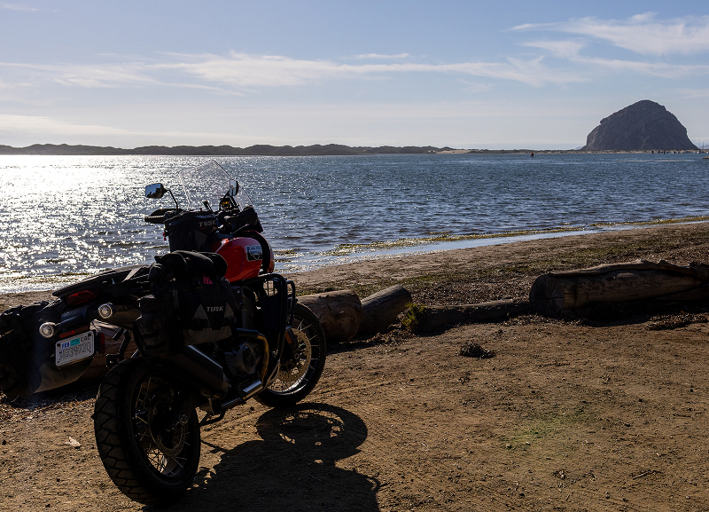 Red H-D Pan America motorcycle parked near calm bay with sandy ground and large coastal rock