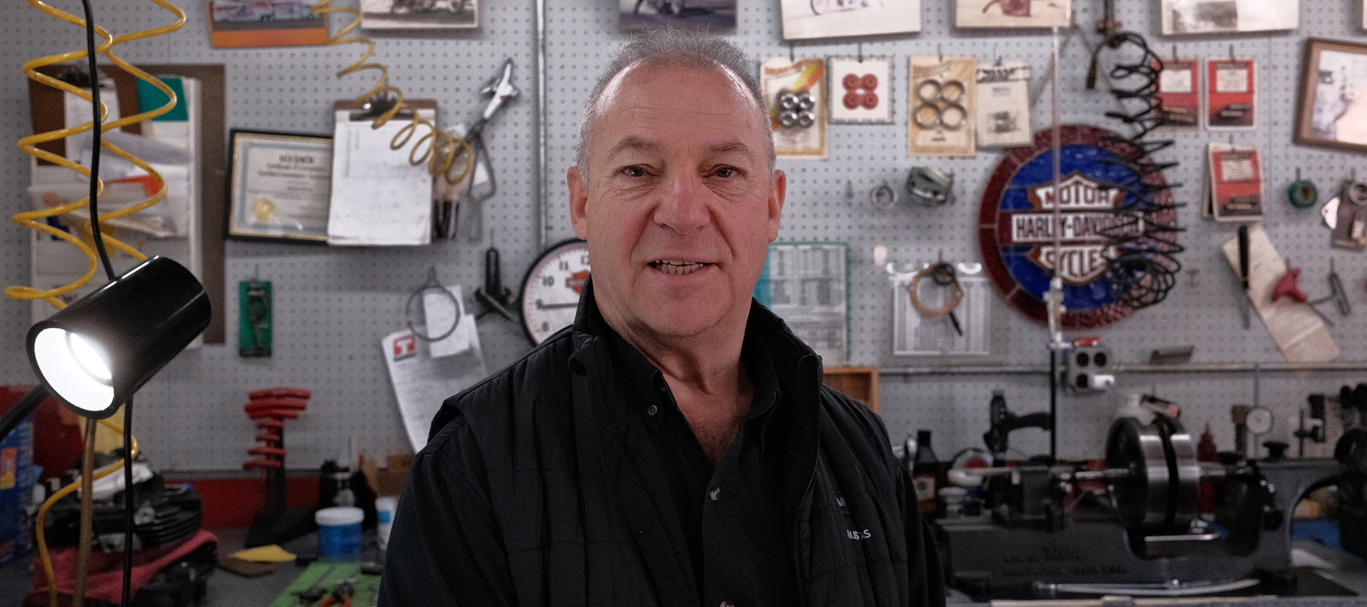 Richie Pilavin standing in service shop in front of pegboard wall with tools and parts