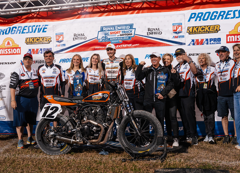 Kody Kopp’s team and crew gather around his race bike posing together in front of sponsor wall after event win