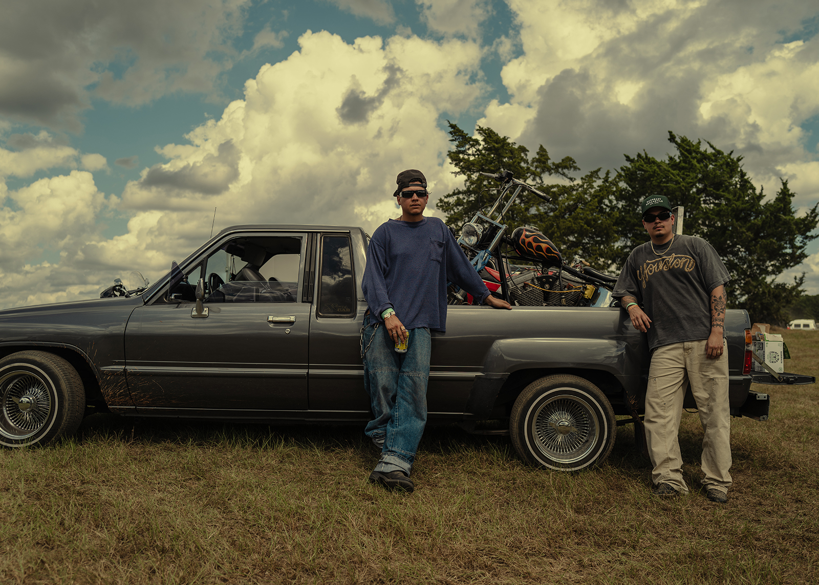 Two men pose next to their small truck lowrider with a custom flame painted chopper in the bed.