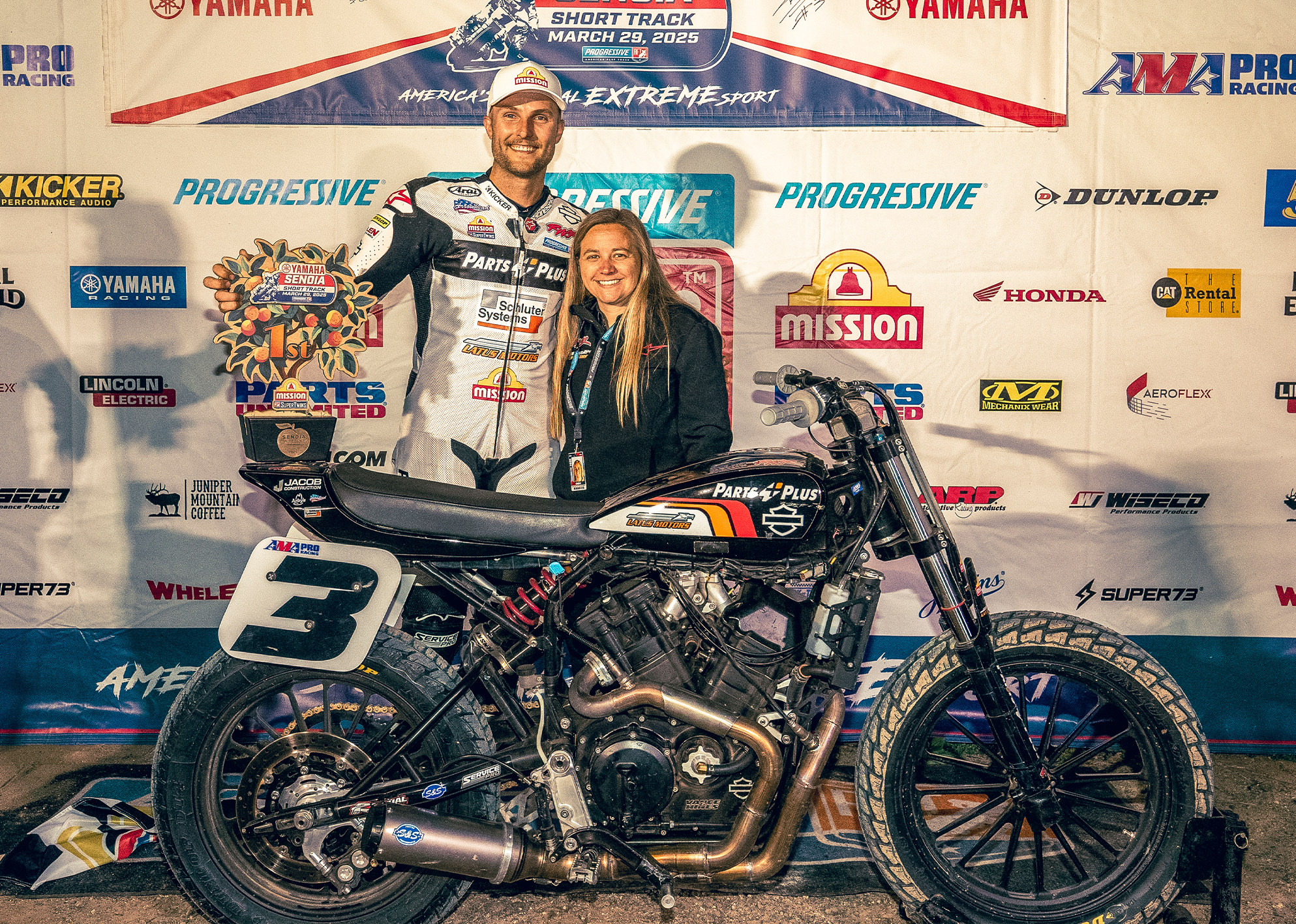 Briar Bauman and his wife Shayna pose with his race motorcycle and a 1st place trophy at a flat track event