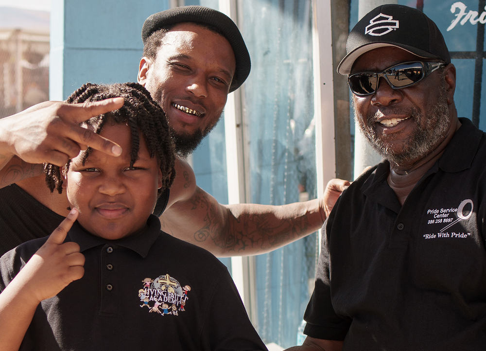 Two adults and a child smile and gesture towards the camera during Daytona Bike Week