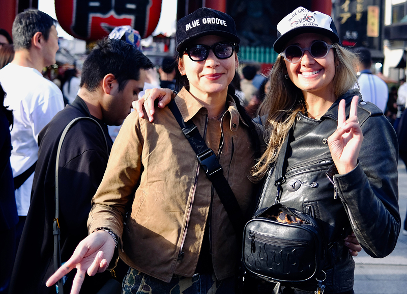 Adri Law and Becky Goebel posing together in a busy outdoor setting with a large red lantern and crowd visible in the background
