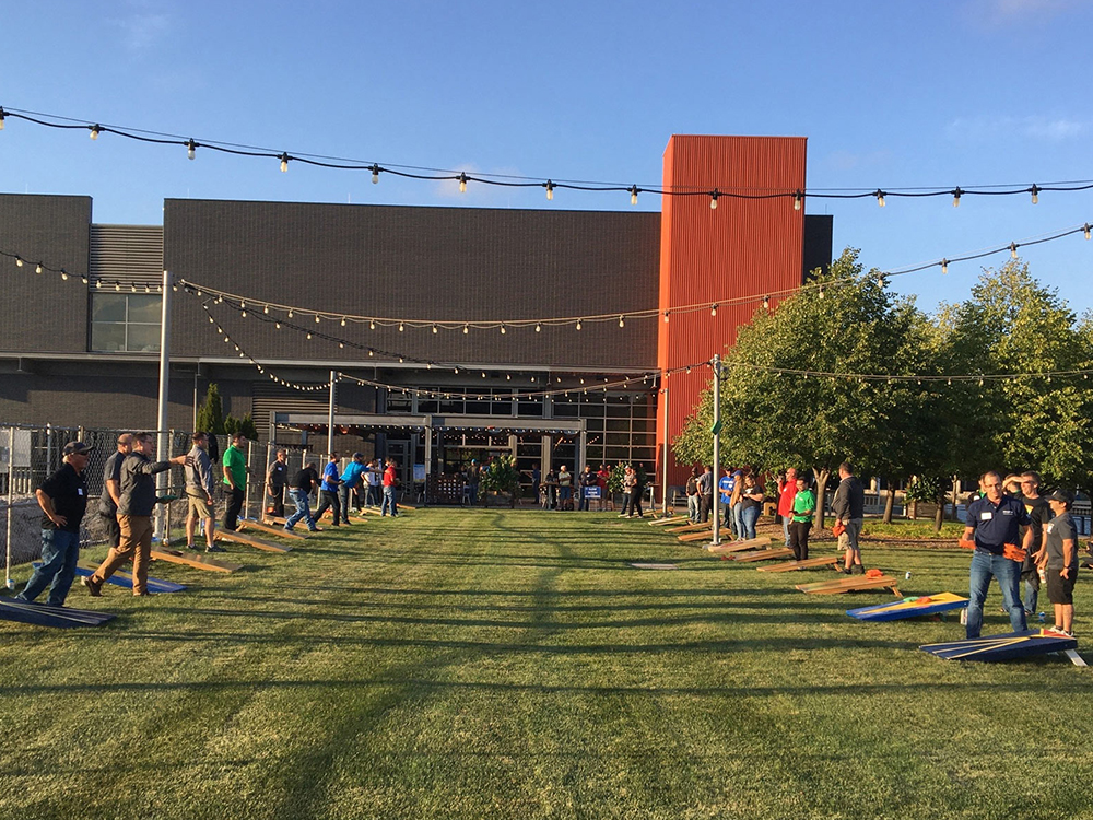 People playing cornhole on lawn outside modern building with string lights