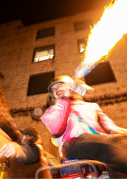 Performer blows a large burst of fire into the air during an outdoor nighttime gathering