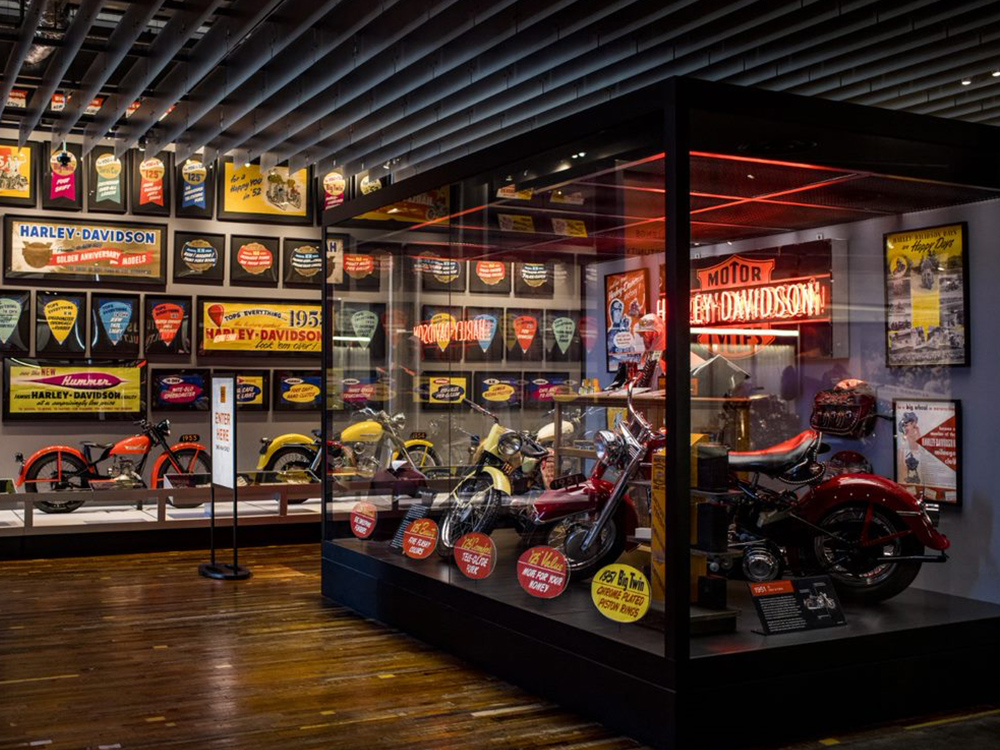 Museum exhibit with vintage Harley-Davidson motorcycles and wall of historic signs