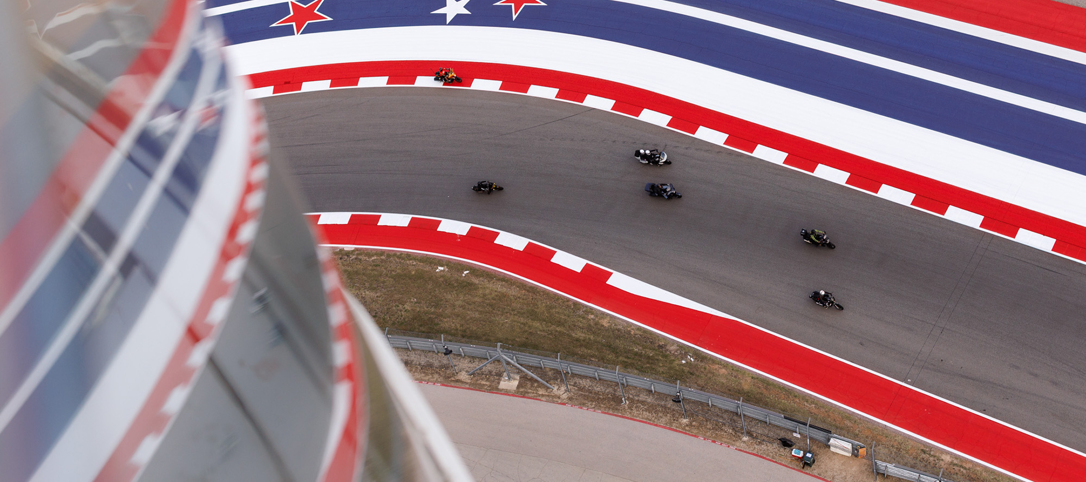Aerial view of motorcycle racers leaning through a sweeping turn on a red white and blue racetrack