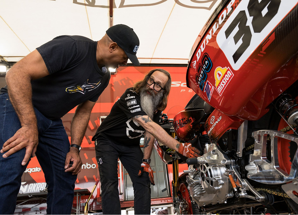 Master mechanic Jason Motal and the author look closely at the engine of a race motorcycle inside a garage during maintenance work