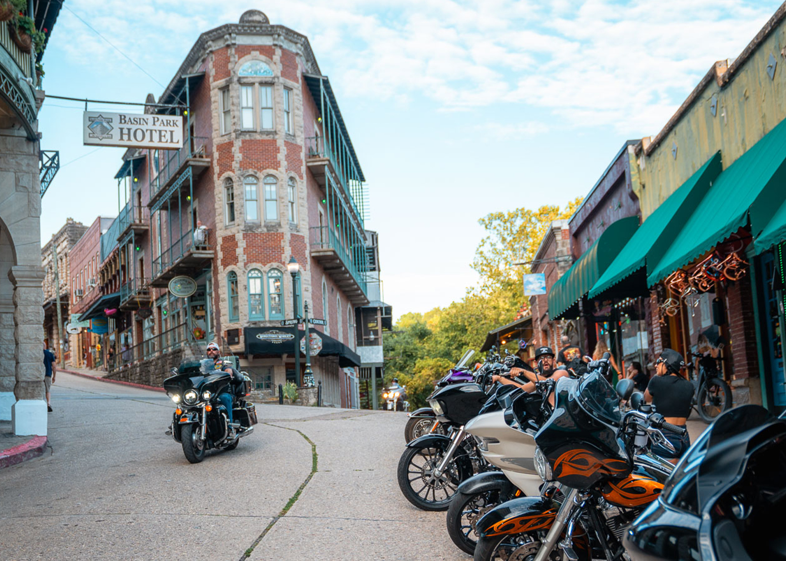 A line of bikes is parked in front of historic buildings while a rider passes on a Street Glide