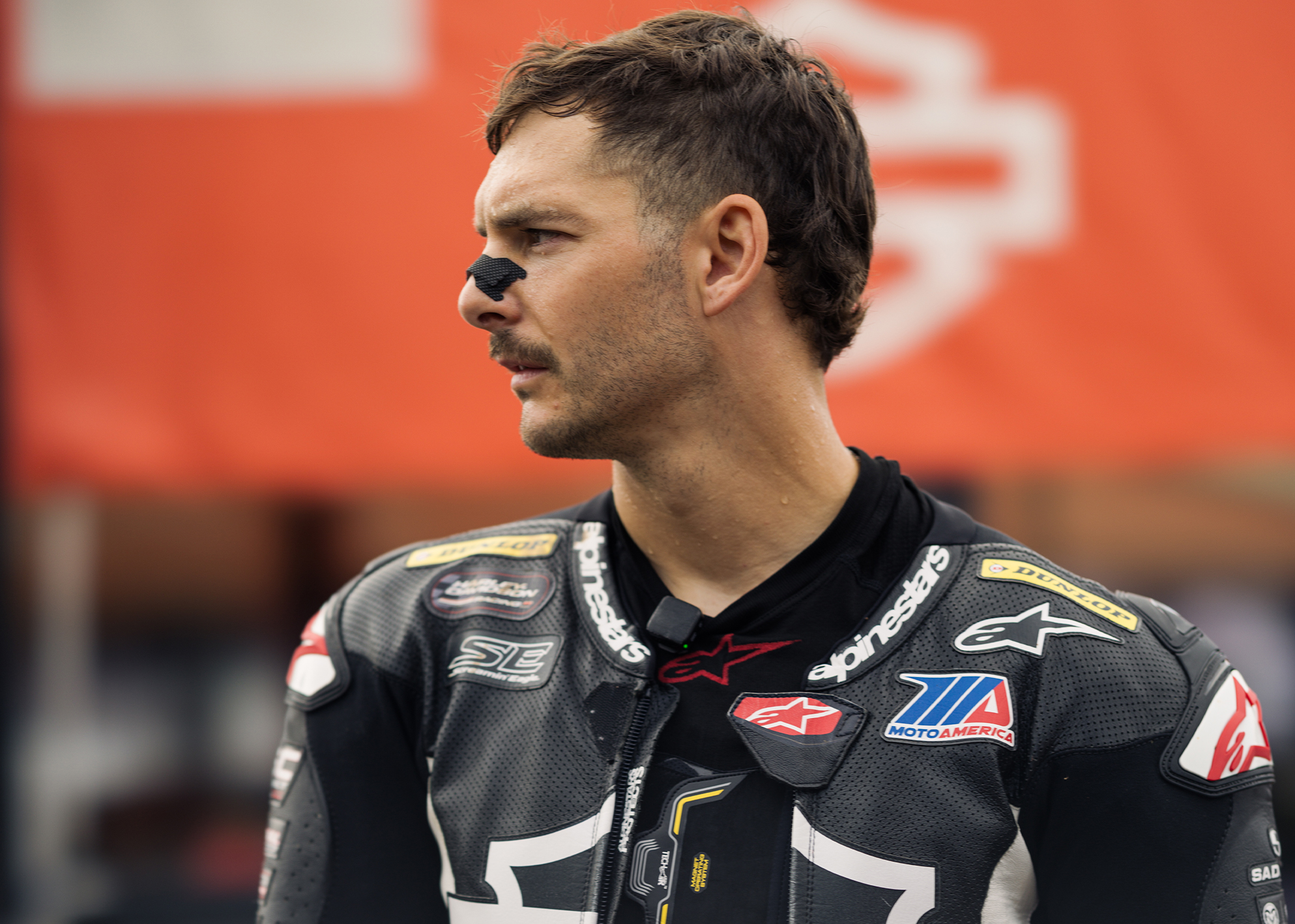 Close-up portrait of James Rispoli in racing leathers, looking to the side with focused expression.