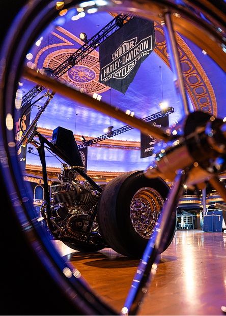 Close‑up of a motorcycle wheel with the show floor and other custom bikes visible through the spokes