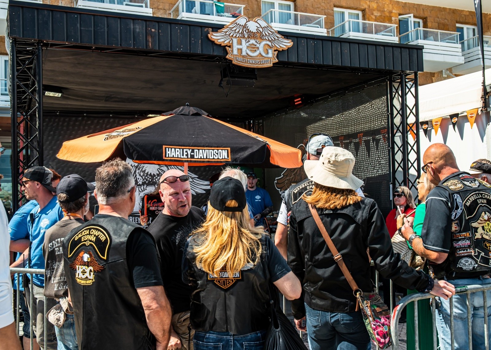 A group of people gathers in front of a branded booth with a winged HOG logo