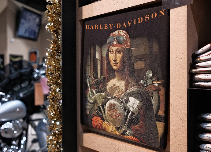 A framed Harley-Davidson t-shirt reimagining the Mona Lisa as a biker wearing a bandana and holding an engine