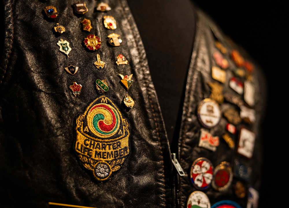 Detailed view of leather vest surface with rows of metal studs, enamel pins, and textured stitching