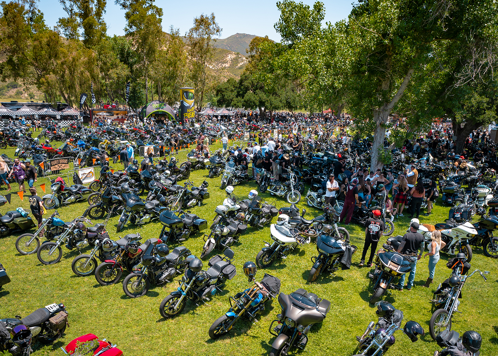 An overhead shot of the event, with hundreds of people and motorcycles parked on the grass in the sunshine.