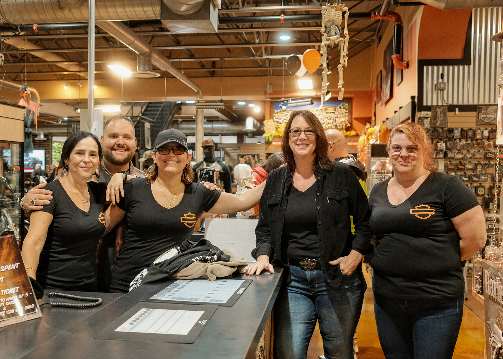 Group of smiling Bergen Harley-Davidson staff posing behind a counter inside the dealership.