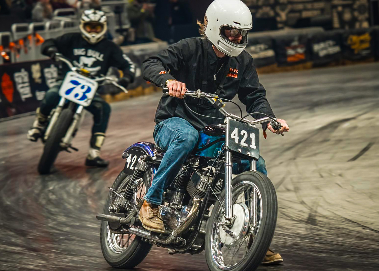 A man puts his foot down in a corner during an indoor flattrack race