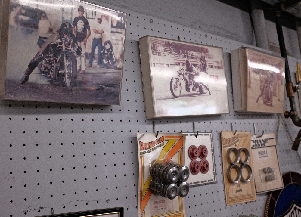 Vintage motorcycle photos and performance parts displayed on pegboard wall inside Precision H-D