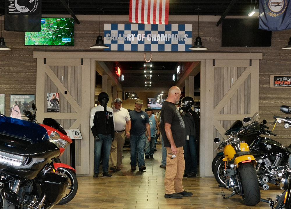 Harley-Davidson showroom entrance with motorcycles, visitors, and a Gallery of Champions checkered sign