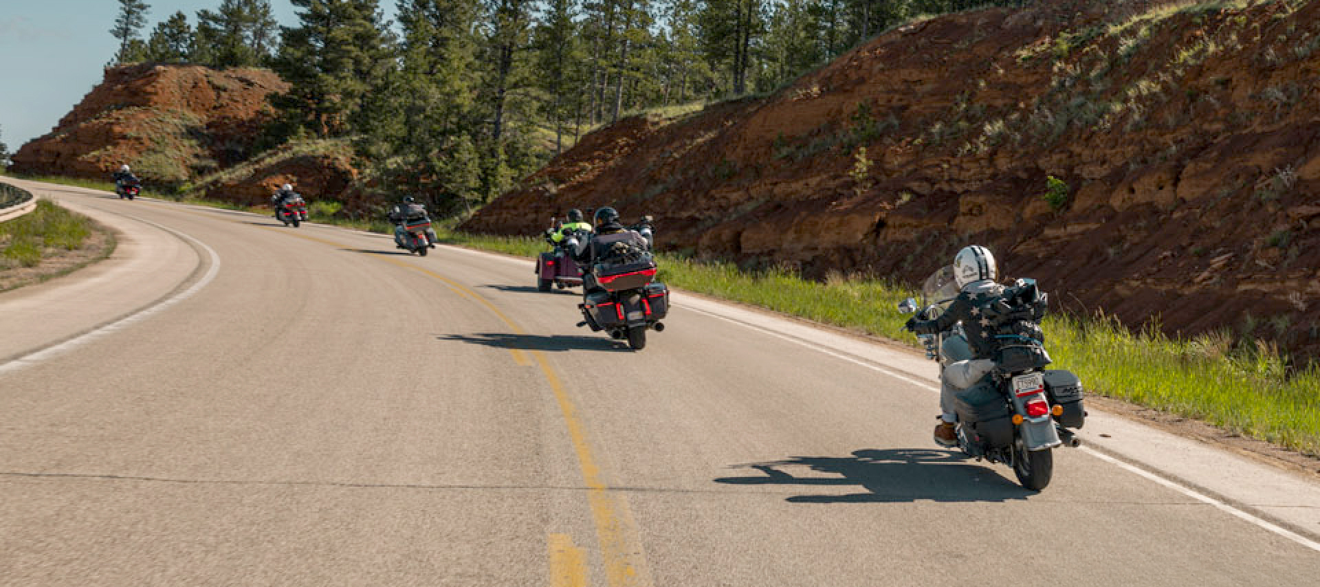 Group of motorcyclists riding on a winding road through a forested area with rocky hills