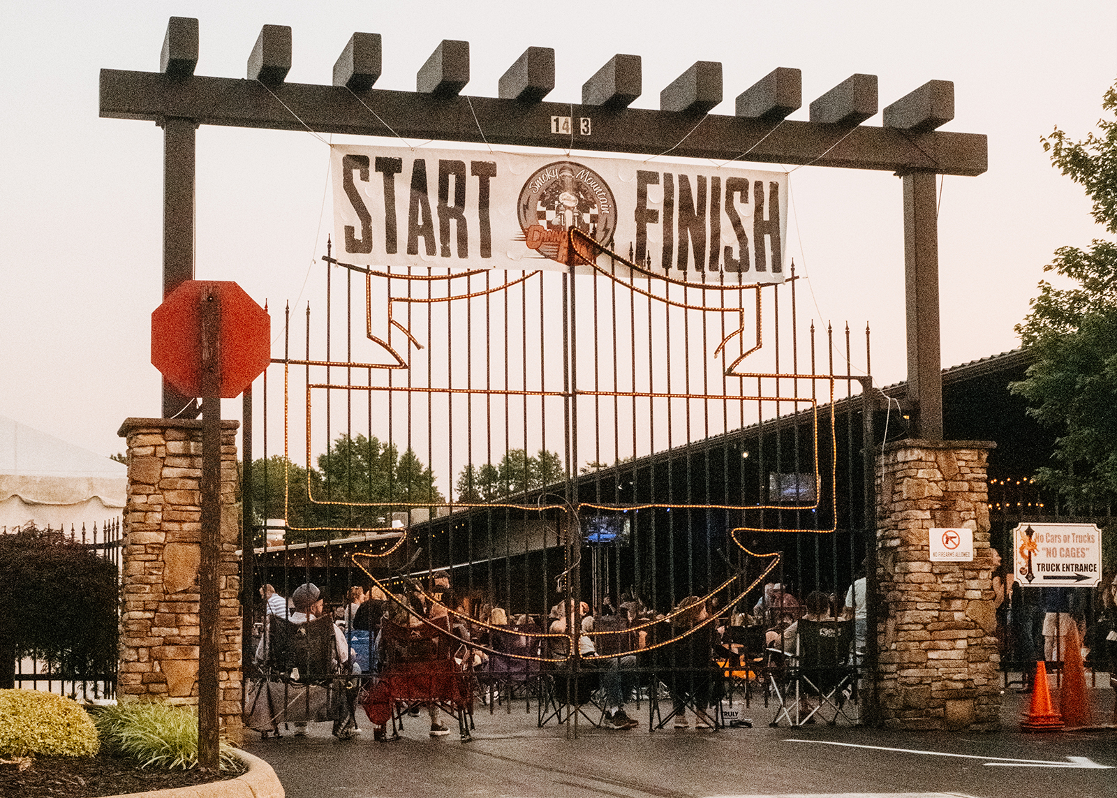 A start and finish line banner hangs above a large gate that is fabricated in the shape of the Harley-Davidson bar and shield logo.