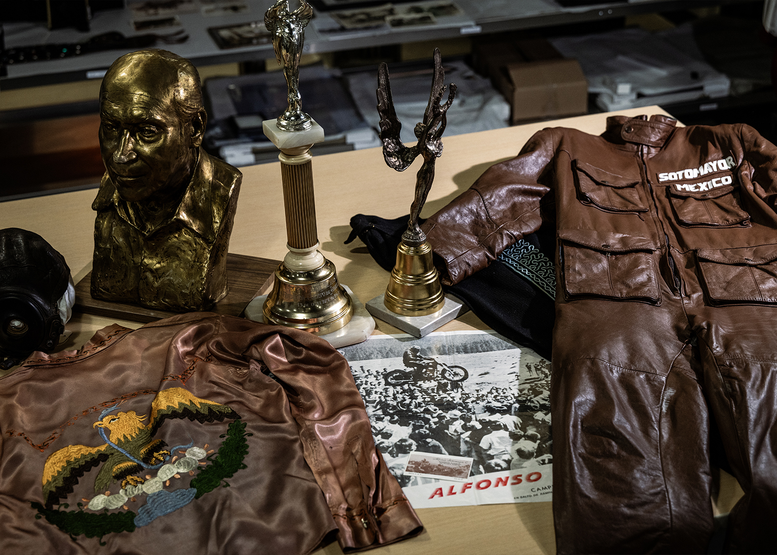 A collection of Alfonso’s memorabilia including trophies, a bust, his brown leather riding suit, and a riding costume with colorful stitching.