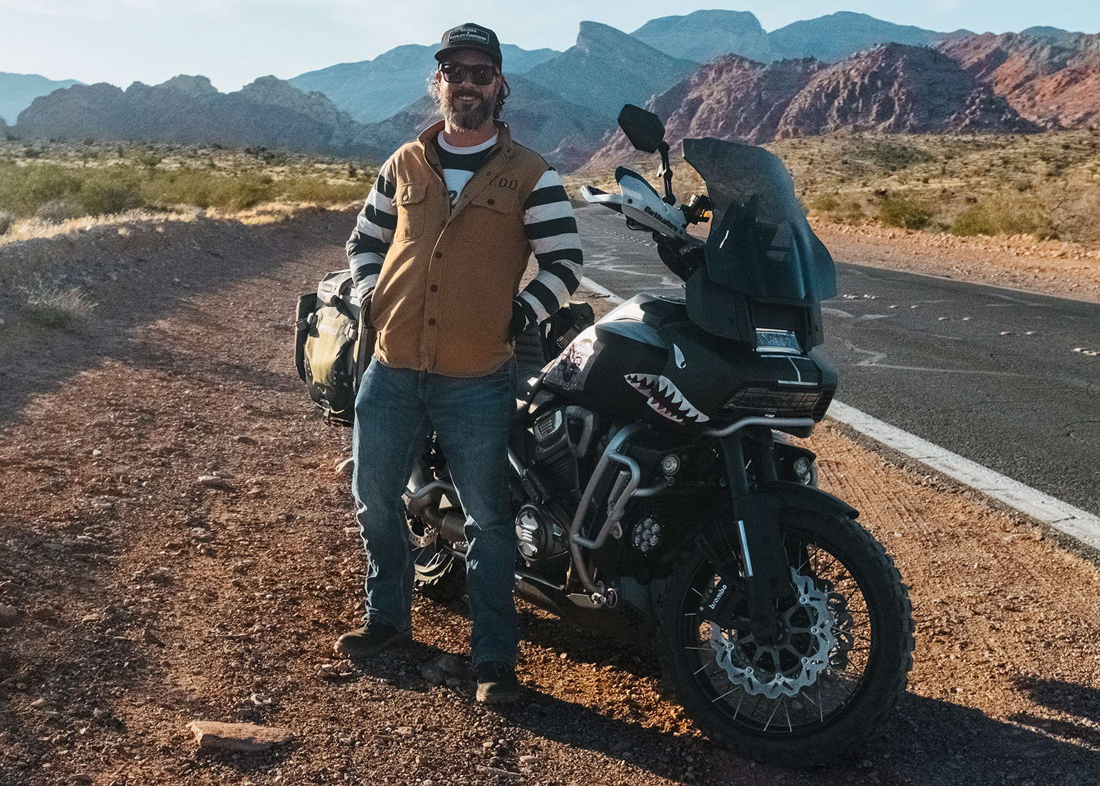 Harley-Davidson Pan America ambassador Justin Edelman poses next to his motorcycle on the side of a desert road.