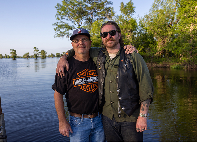 Payton and Barry Broussard stand arm in arm at the water’s edge, with cypress trees and calm swamp water behind them
