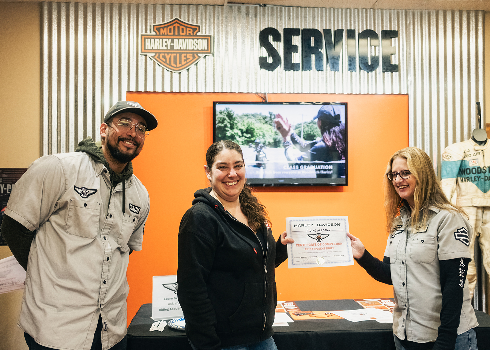 Two instructors award a student with a H-D Riding Academy certificate of completion.