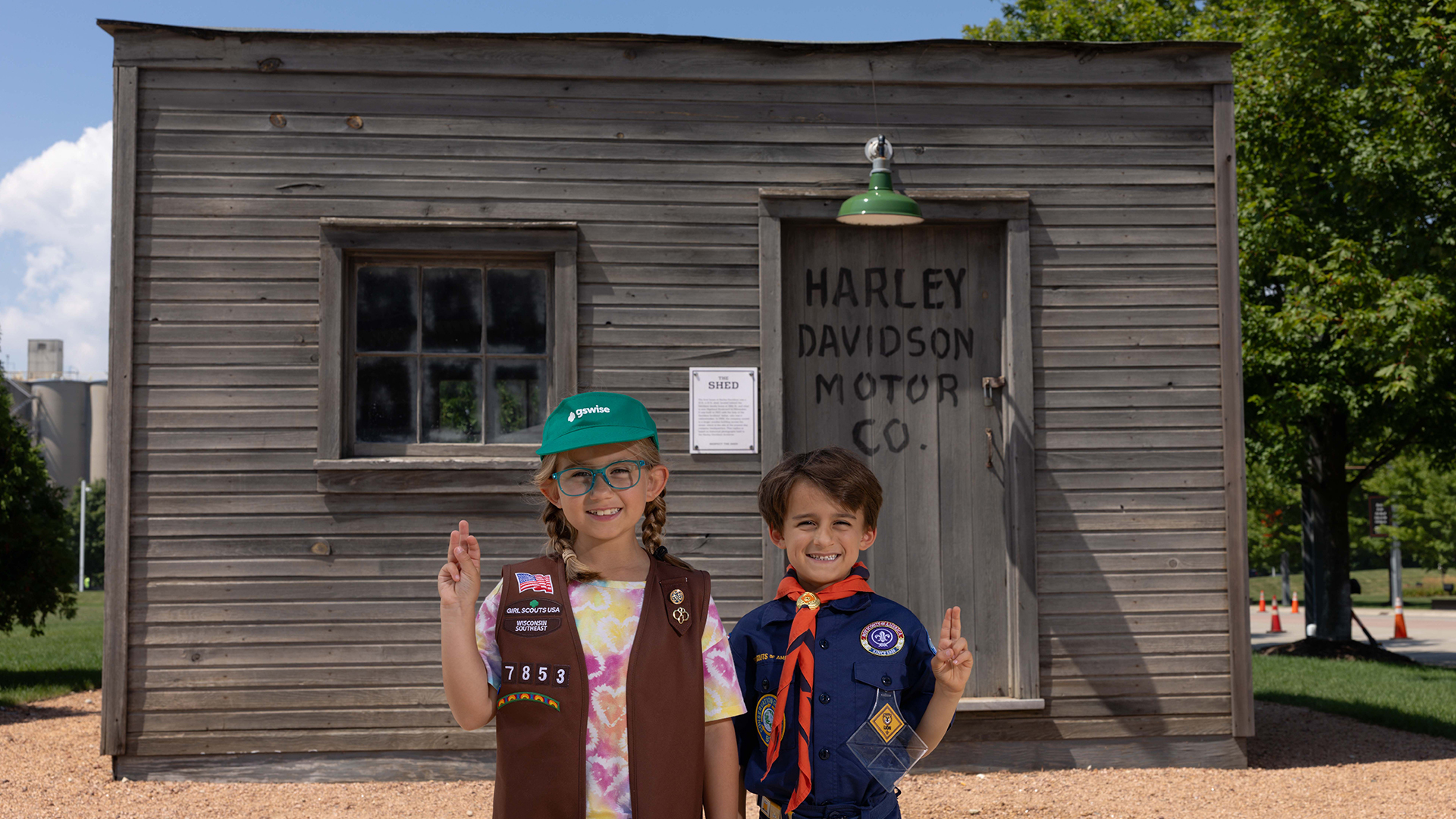 Two children in scout uniforms posing in front of Harley-Davidson Motor Co. building