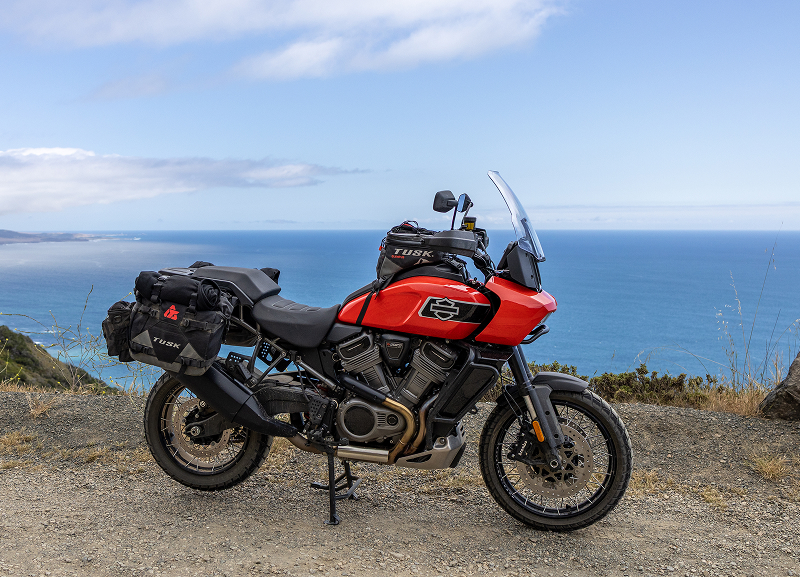 Red H-D Pan America motorcycle with luggage parked on coastal bluff overlooking blue ocean and horizon