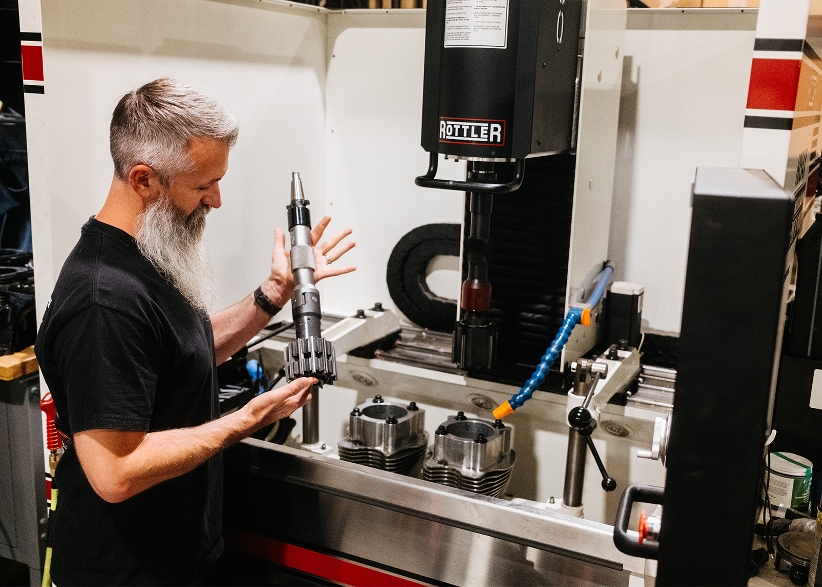 Moonshine Harley-Davidson Owner and General manager Jamie Lima holds a specialized machining tool in front of a Rottler engine boring machine.