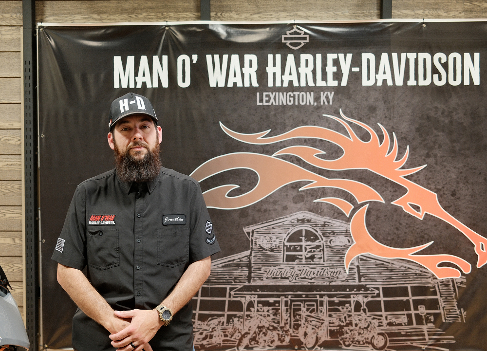 Man O’ War Harley-Davidson General Manager Jonathan Urzua stands before a dealership banner featuring the iconic horse logo