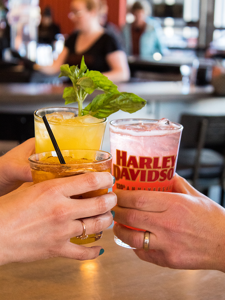 Hands clinking colorful cocktails in glasses at bar counter