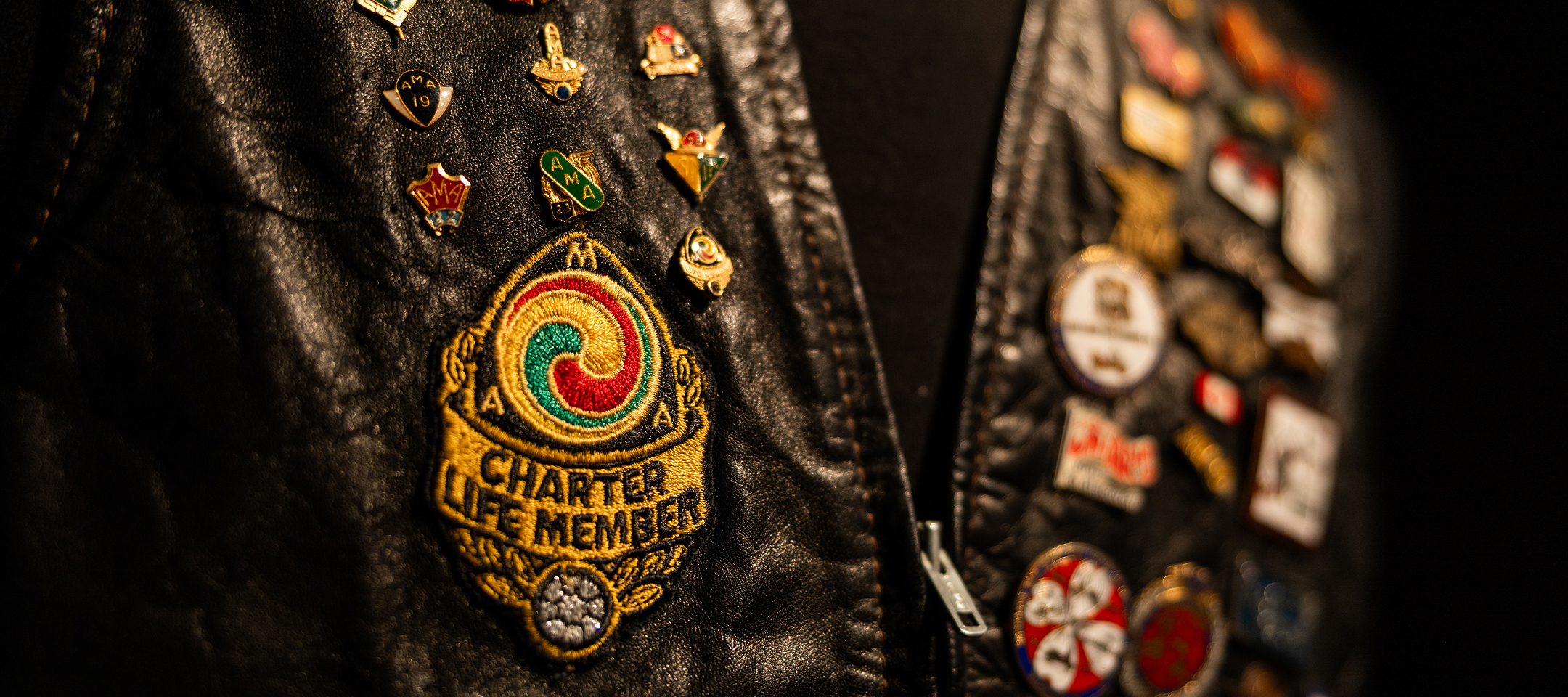 Close-up of black leather vest covered in pins, featuring a colorful embroidered Charter Life Member AMA patch