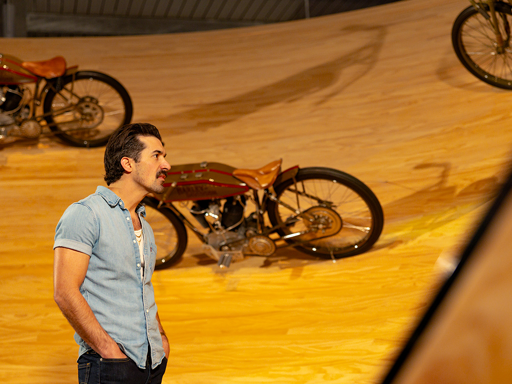 Visitor observing vintage motorcycles displayed on curved wooden exhibit