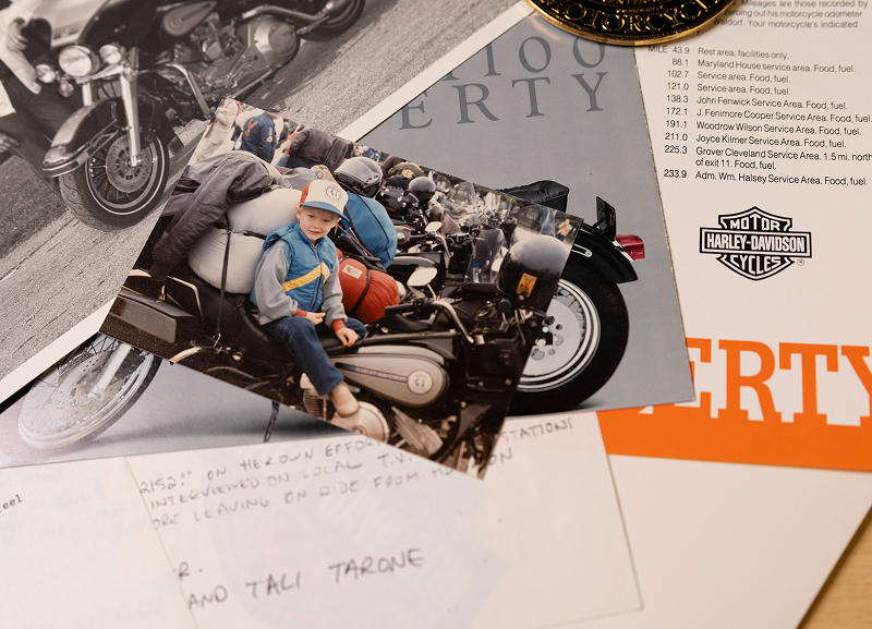 Printed color photo of young child on a Harley-Davidson motorcycle layered over Liberty Centennial papers