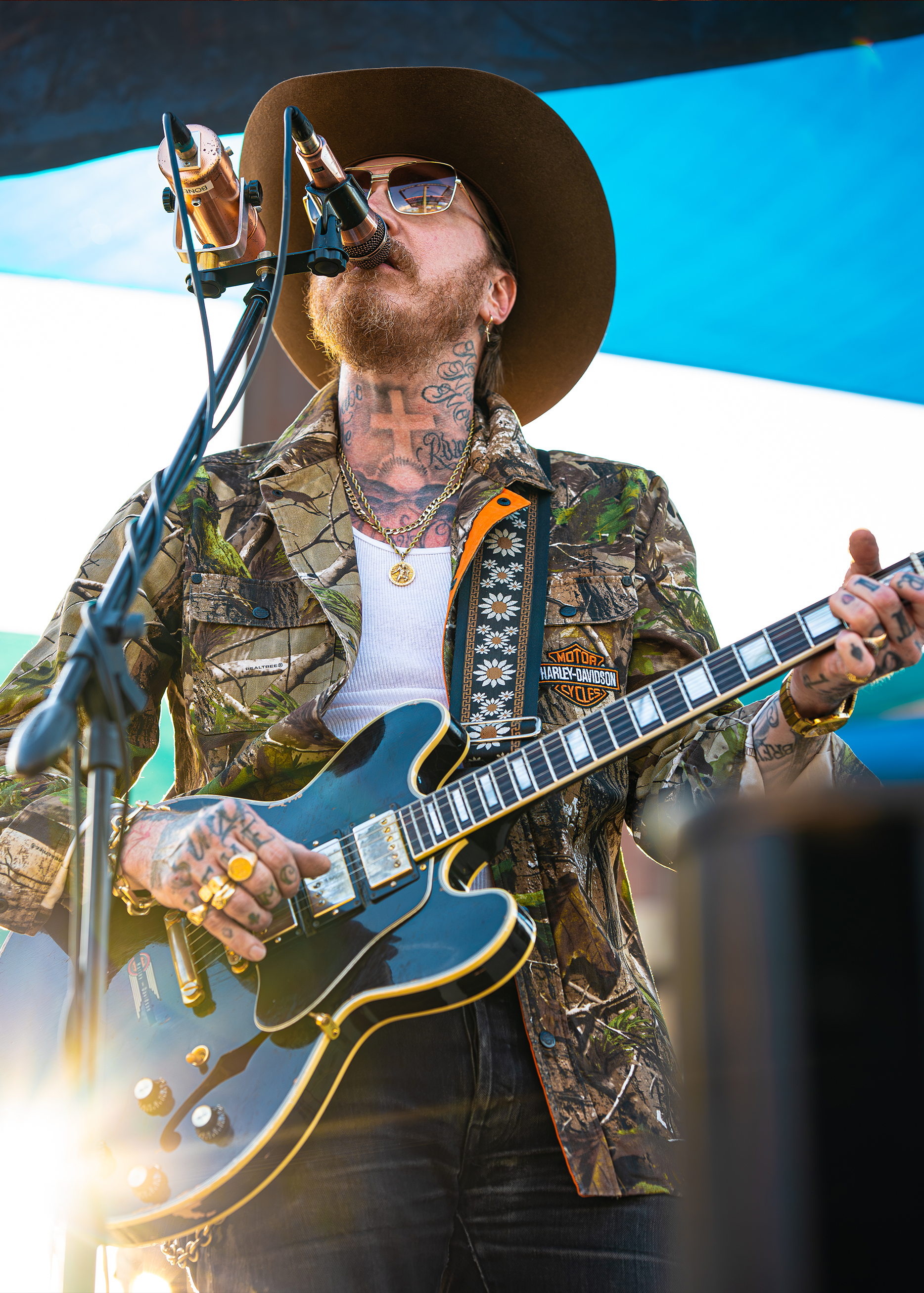 Artist Bones Owens sings and plays guitar on stage wearing a Harley-Davidson x Realtree camo shirt.