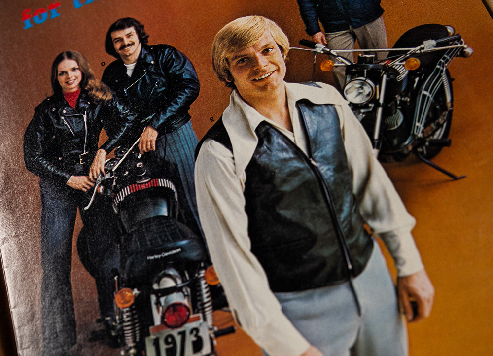 Vintage photo of motorcycle riders posed beside a bike, wearing leather jackets and layered riding gear