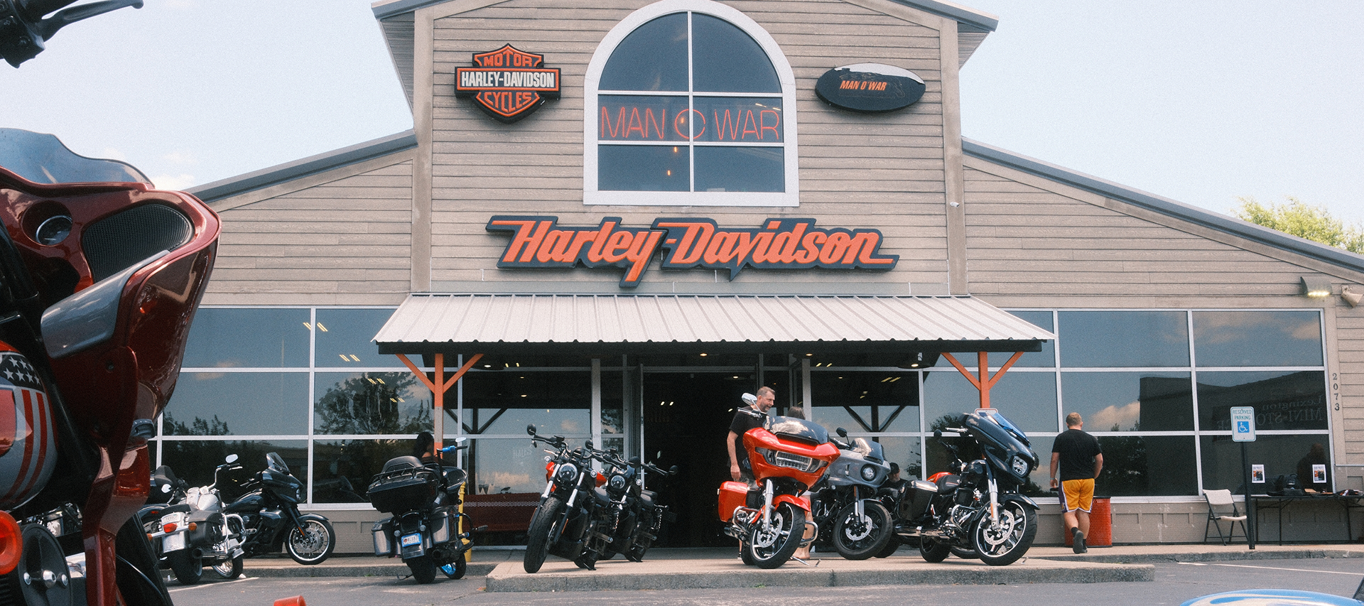 Man O’ War Harley-Davidson dealership storefront with touring motorcycles parked outside and riders gathering near the entrance